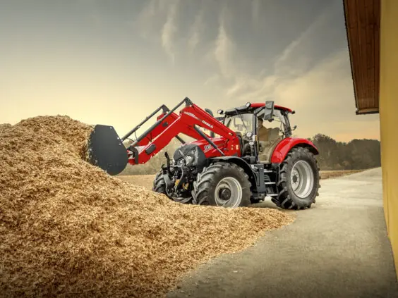 Rød traktor fra Case IH Maxxum-serien med frontlaster som arbeider i en haug med flis.