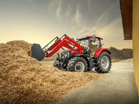 Rød traktor fra Case IH Maxxum-serien med frontlaster som arbeider i en haug med flis.