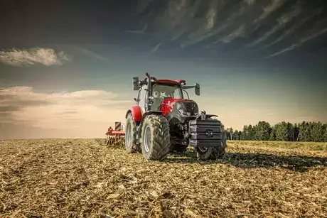 Rød traktor fra Case IH Maxxum-serien i arbeid på en innhøstet åker under dramatisk himmel.