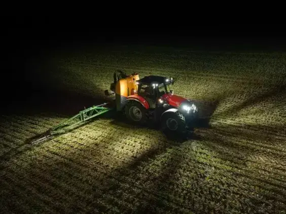Rød traktor fra Case IH Maxxum-serien i arbeid på en mørk åker om natten.