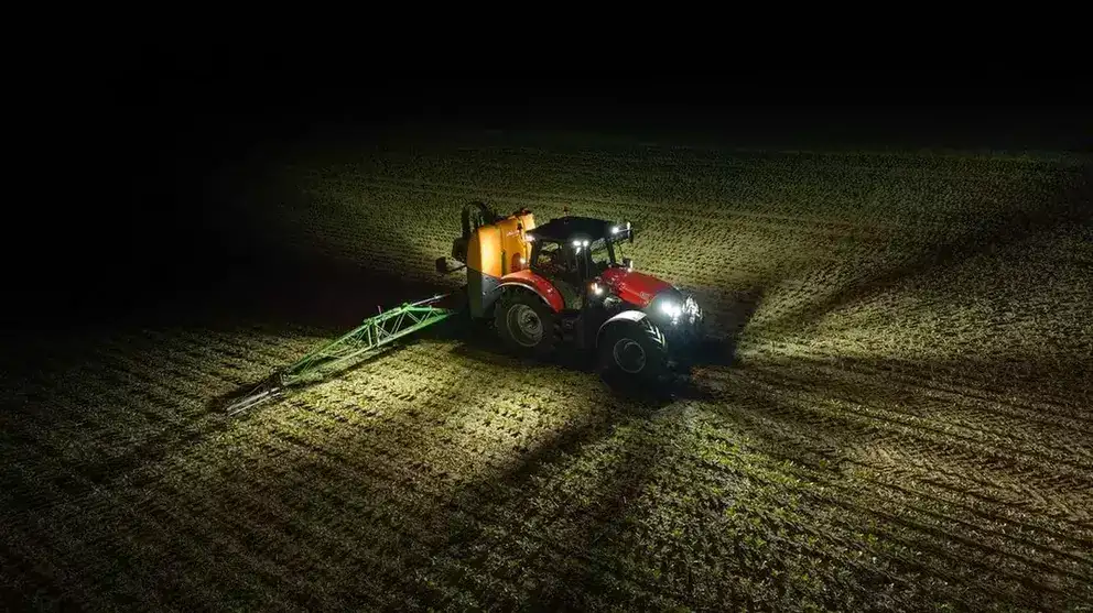 Rød traktor fra Case IH Maxxum-serien i arbeid på en mørk åker om natten.