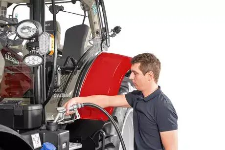 En mann fyller drivstoff på en rød Case IH traktor ved bruk av en fyllepistol.