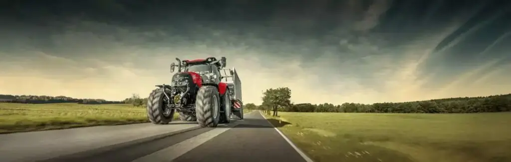Rød traktor fra Case IH Maxxum-serien kjører på en vei i et åpent landskap.