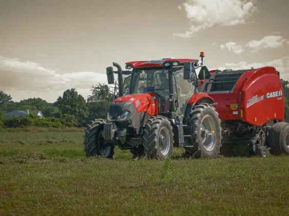 Rød traktor fra Case IH Maxxum-serien med rundballepresse i arbeid på en gressmark.