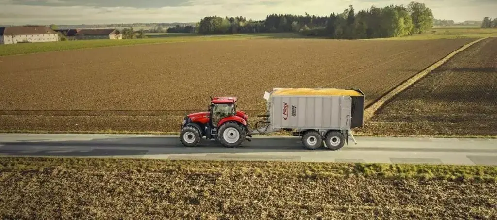 En rød Case IH traktor trekker en Fliegl tilhenger fylt med korn langs en vei.