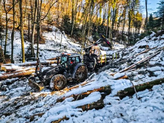 Traktor med PALMS 15U tømmervogn laster tømmerstokker i et snødekket skogsterreng.