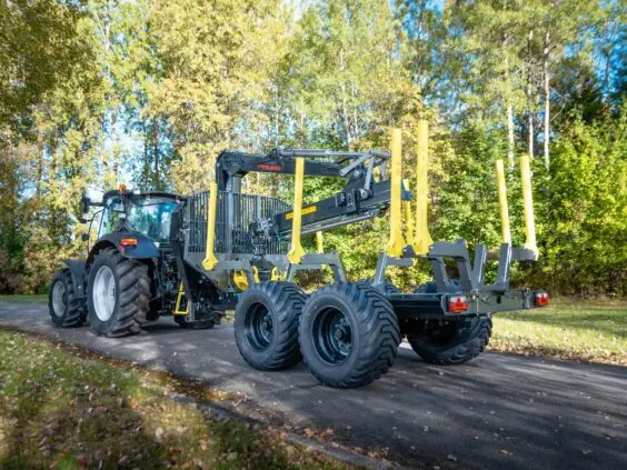 Traktor med tømmervogn utstyrt med en robust PALMS 7.87 skogskran på en vei.