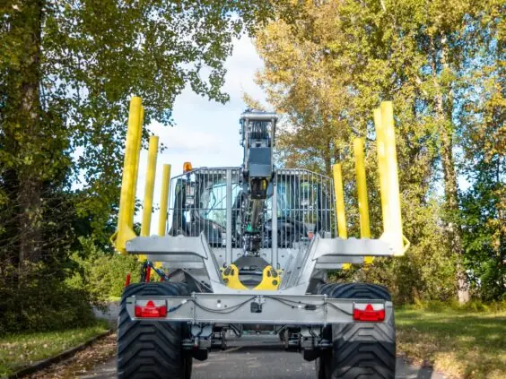 En robust PALMS 7.87 skogskran på tømmervogn parkert på en vei omgitt av høsttrær.