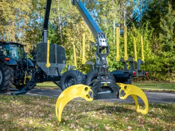 En PALMS 7.87 skogskran med gul tømmerklo montert på tømmervogn foran en skog.