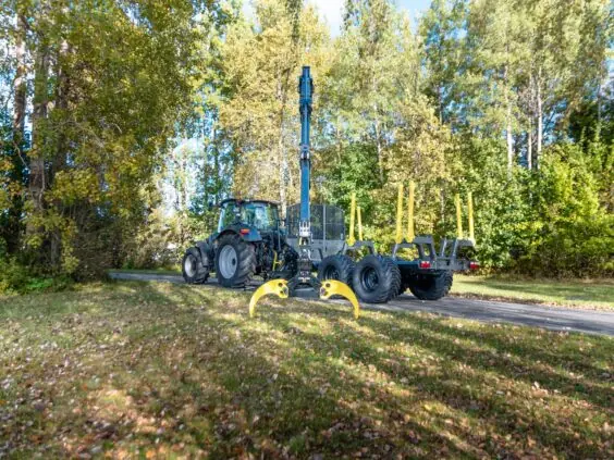 Traktor med tømmertilhenger og PALMS 7.87 skogskran parkert på en skogvei.