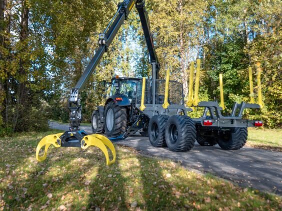 En PALMS 7.87 skogskran montert på en tømmervogn bak en traktor i skogen.