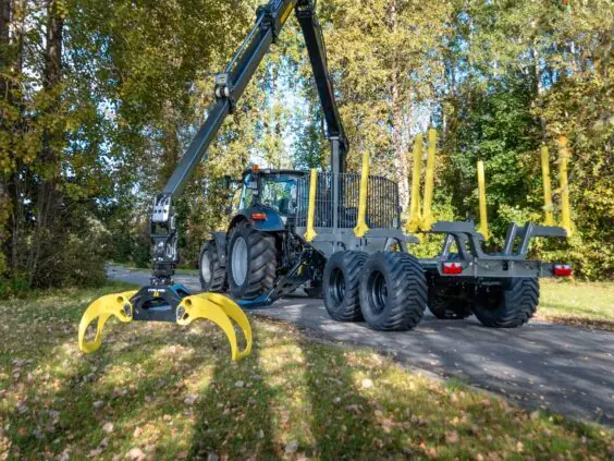 En PALMS 7.87 skogskran montert på en tømmervogn bak en traktor i skogen.