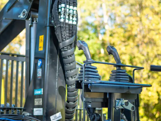Nærbilde av kontrollspaker og hydraulikkslanger på en PALMS 7.87 skogskran i skogen.