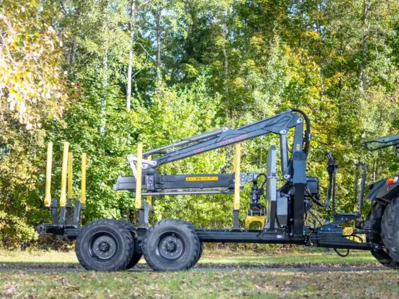 En robust PALMS 7.87 skogskran montert på en tømmertilhenger foran en skog.