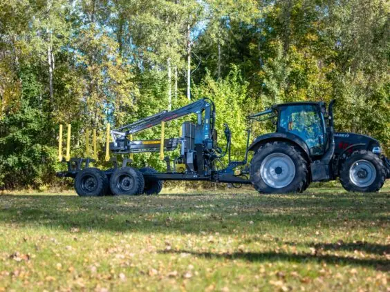 Svart traktor koblet til en tømmertilhenger med PALMS 7.87 skogskran foran grønn skog.