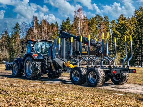 Svart traktor tilkoblet en PALMS 15U tømmervogn på en vei foran en skog.