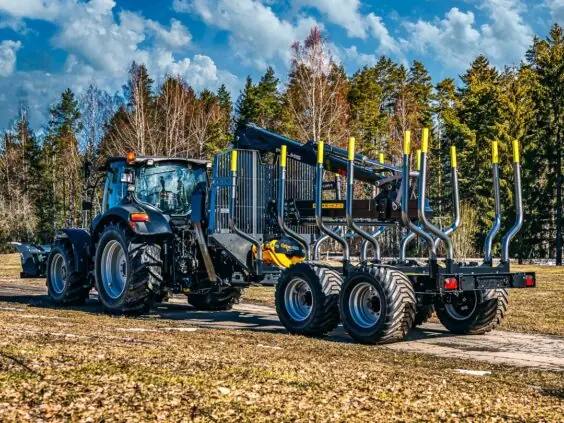 Svart traktor tilkoblet en PALMS 15U tømmervogn på en vei foran en skog.