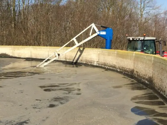 En hvit ØRUM GMD-8600 gjødselmikser montert i en gjødselkum med en traktor i bakgrunnen.