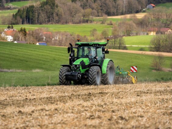 Grønn Deutz-Fahr Series 5 traktor som arbeider på et jorde i et kupert landskap.