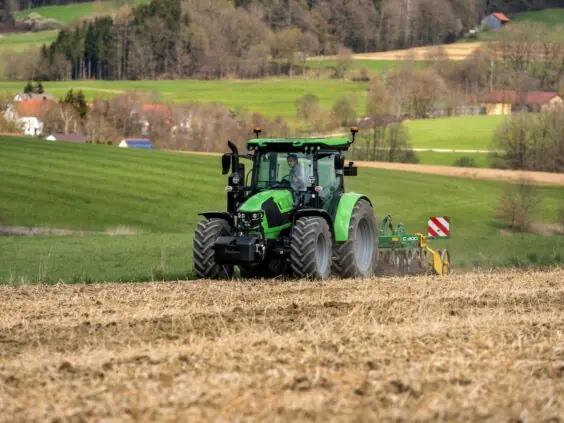 Grønn Deutz-Fahr Series 5 traktor som arbeider på et jorde i et kupert landskap.