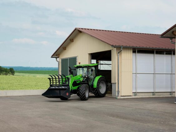 Grønn Deutz-Fahr Series 5 traktor med frontlaster ved en moderne gårdsbygning i et åpent landskap.