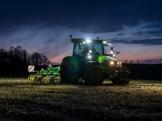 Grønn Deutz-Fahr Series 5 traktor med skarpe lys i arbeid på en åker ved skumring.