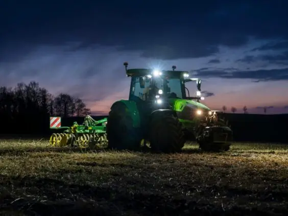 Grønn Deutz-Fahr Series 5 traktor med skarpe lys i arbeid på en åker ved skumring.