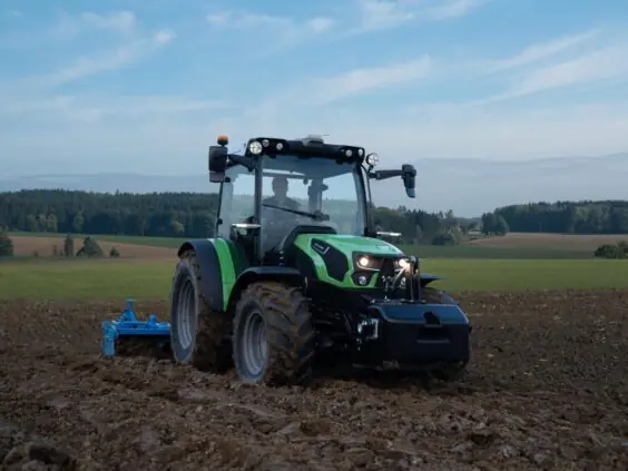 Grønn Deutz-Fahr Series 5D TTV traktor som arbeider på en åker under blå himmel.