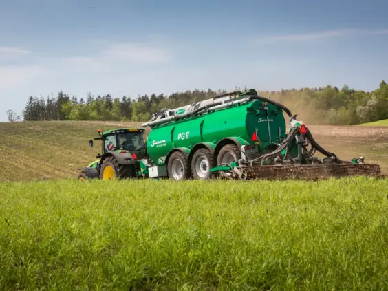 En grønn traktor som trekker en SAMSON PG II gjødselvogn på en grønn åker.