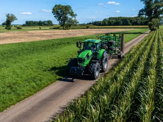 Grønn Deutz-Fahr Series 8 traktor som kjører på en landevei ved siden av en maisåker.