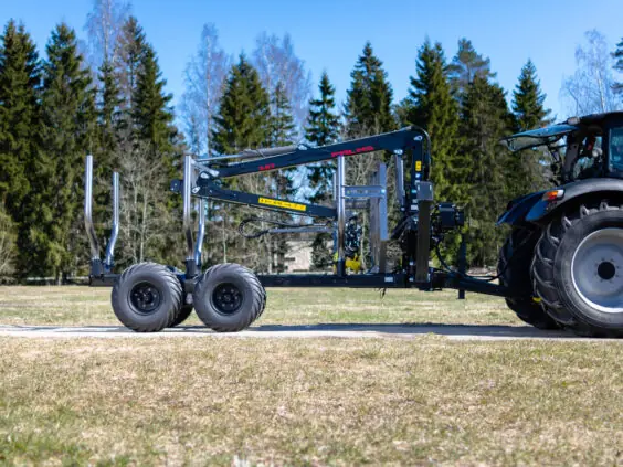 En robust PALMS 8D tømmervogn med kran koblet til en traktor på en eng.