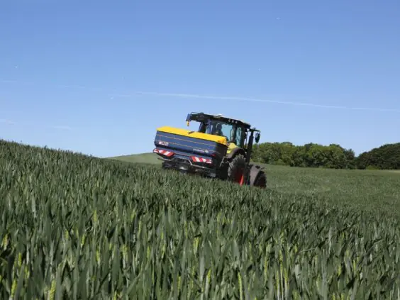 En traktor med Bogballe M35 base kunstgjødselspreder i en grønn åker under blå himmel.
