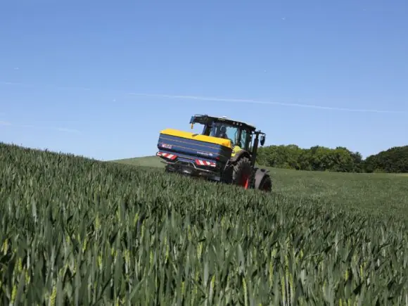 En traktor med Bogballe M35 base kunstgjødselspreder i en grønn åker under blå himmel.