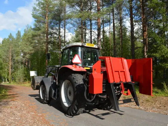 En rød traktor på skogsvei med Hakki Pilke HH 110 vedmaskin montert bak.