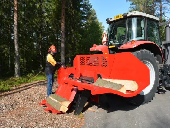 En operatør som bruker Hakki Pilke HH 110 vedmaskin montert på en rød traktor.