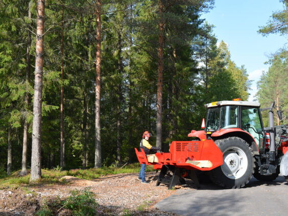 Rød Hakki Pilke HH 110 vedmaskin koblet til traktor i skogen under vedkløyving.