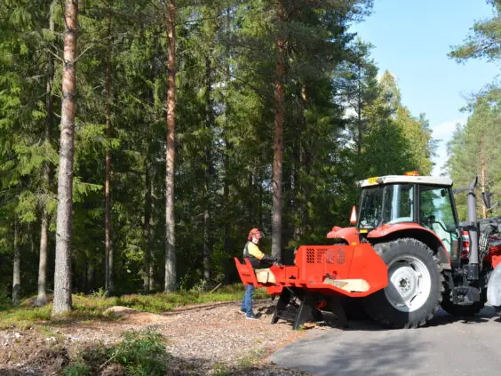 Rød Hakki Pilke HH 110 vedmaskin koblet til traktor i skogen under vedkløyving.