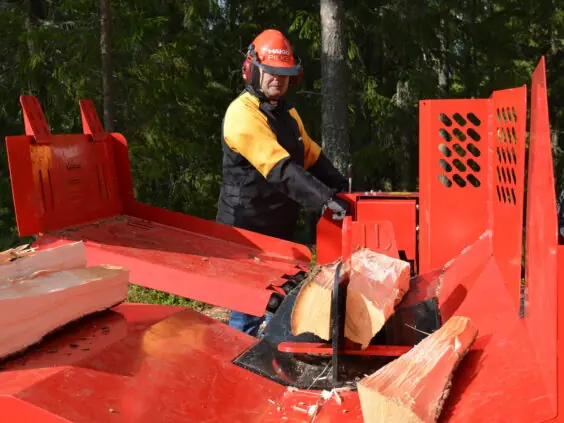 En mann som betjener en rød Hakki Pilke HH 110 vedmaskin i skogen.