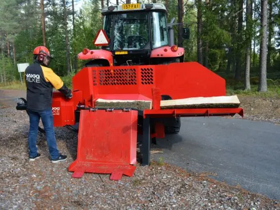 En mann som betjener en rød Hakki Pilke HH 110 vedmaskin montert på traktor.