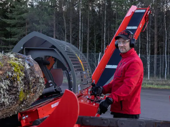 En mann i rød jakke som betjener en Hakki Pilke 43 vedmaskin utendørs.