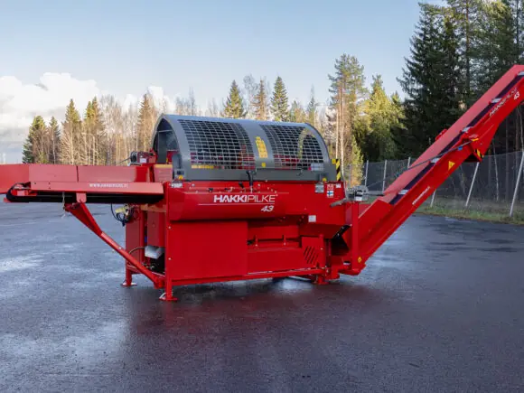 Rød Hakki Pilke 43 vedmaskin på asfaltert flate med skog i bakgrunnen.