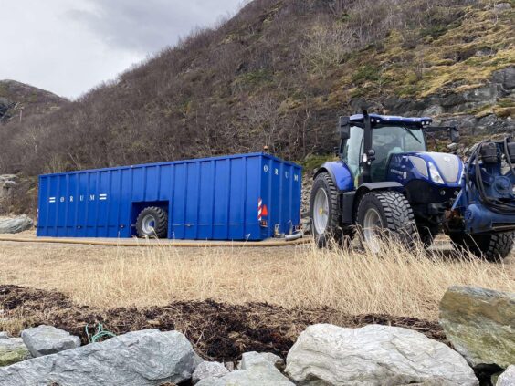 Blå Ørum Buffertank 100 på et tørt jorde ved siden av en blå traktor.