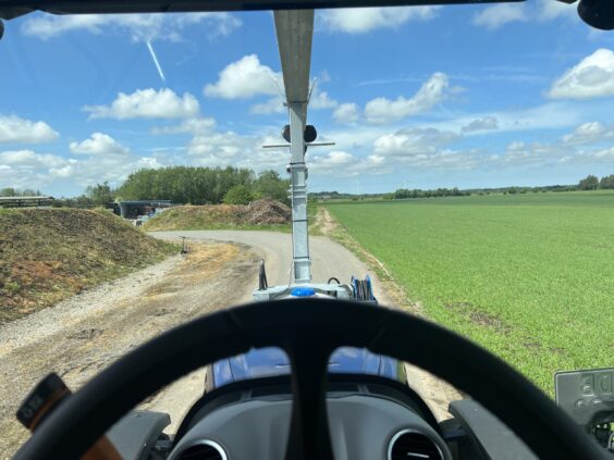 Traktor med ØRUM GMD-8600 gjødselmikser sett fra førerhuset i et åpent jordbrukslandskap.