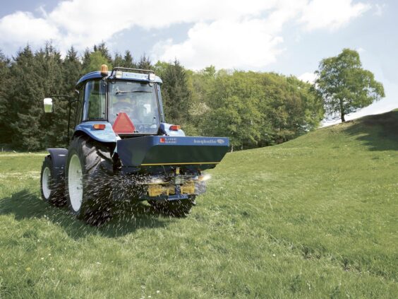 Blå traktor i arbeid på en grønn eng med Bogballe L15 base kunstgjødselspreder.