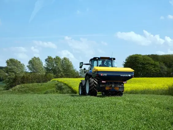 En blå traktor med Bogballe L15 plus kunstgjødselspreder i en grønn åker.