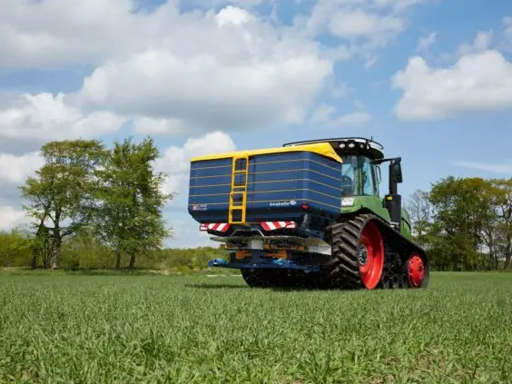 En traktor med en Bogballe M60W plus kunstgjødselspreder kjører på en grønn åker.
