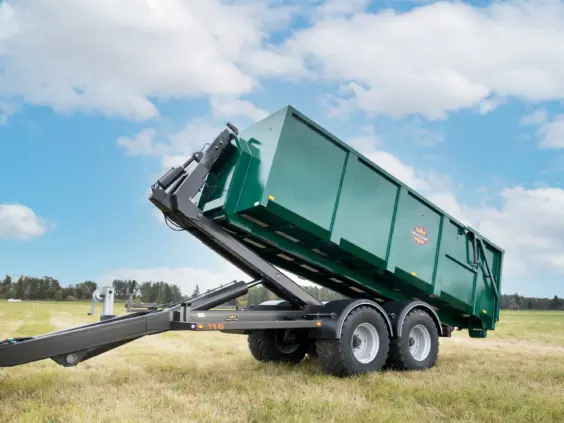 Grønn ML115S krokløfthenger med hevet container stående på en åker under blå himmel.
