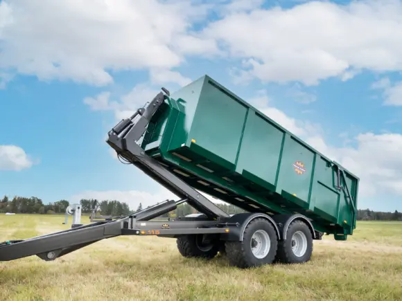 Grønn ML115S krokløfthenger med hevet container stående på en åker under blå himmel.