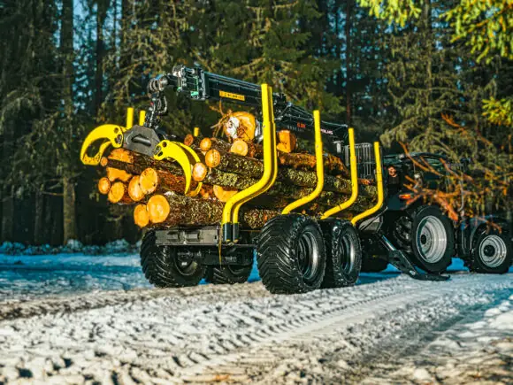 En fullastet PALMS 14U tømmervogn trekkes av en traktor på en snødekt skogsvei.