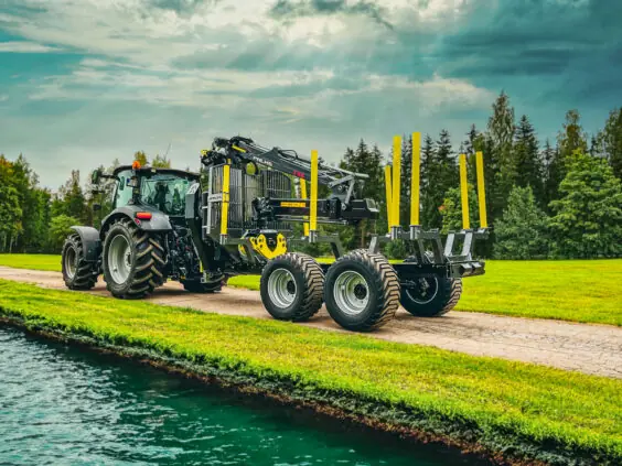 Svart traktor som trekker en PALMS 12U tømmervogn på en vei ved vannet.